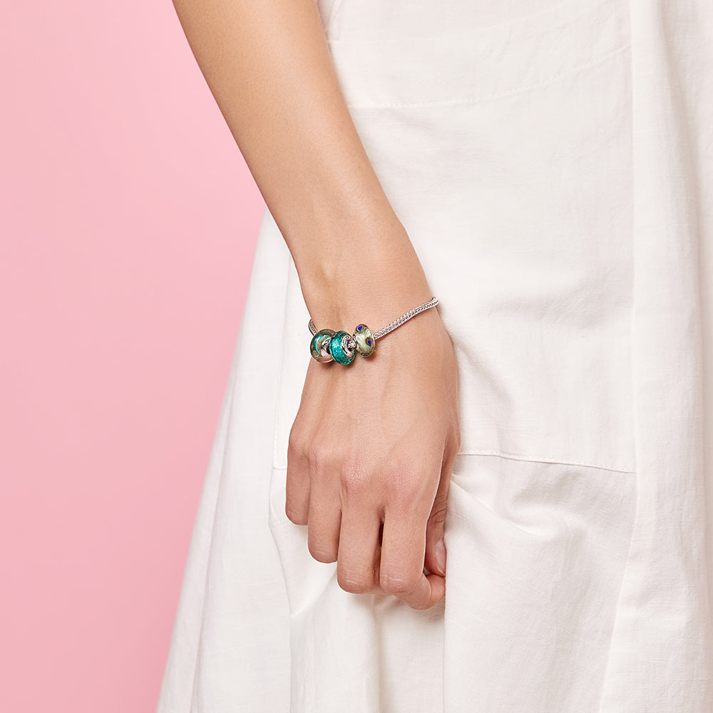 Woman wearing ATHENAIE silver charm bracelet with Murano beads